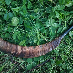 May include: A handcrafted horn, likely for drinking or ceremonial use, with a dark, polished finish on the mouthpiece and a natural, striped pattern on the body. The horn is lying on a bed of green grass and clover.