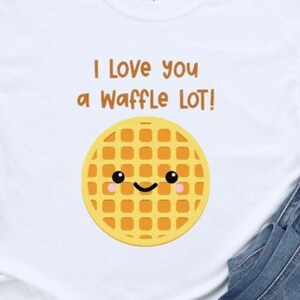 May include: White t-shirt with the phrase "I love you a Waffle LOT!" and a smiling waffle graphic. The shirt is paired with blue denim jeans and white Converse sneakers.