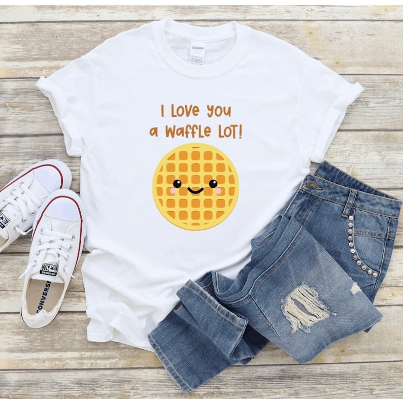 May include: White t-shirt with the phrase "I love you a Waffle LOT!" and a smiling waffle graphic. The shirt is paired with blue denim jeans and white Converse sneakers.