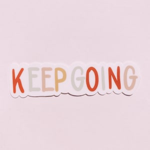 Puede incluir: Una pegatina blanca con las palabras "KEEP GOING" en letras de colores. Las letras son en tonos de naranja, amarillo, azul claro y gris.