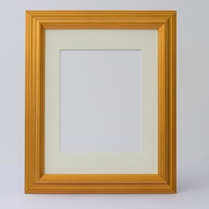 May include: A gold picture frame with a white mat. The frame has a simple, classic design.