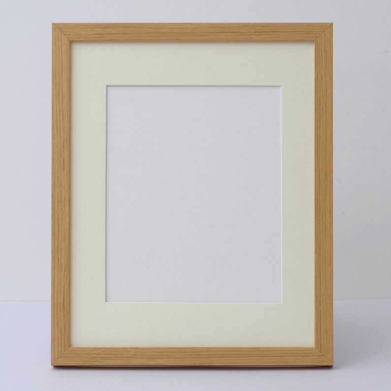 May include: A rectangular picture frame with a light wood grain finish. The frame has a cream-colored mat and a white interior space for a photo or artwork. The frame is designed for displaying images.