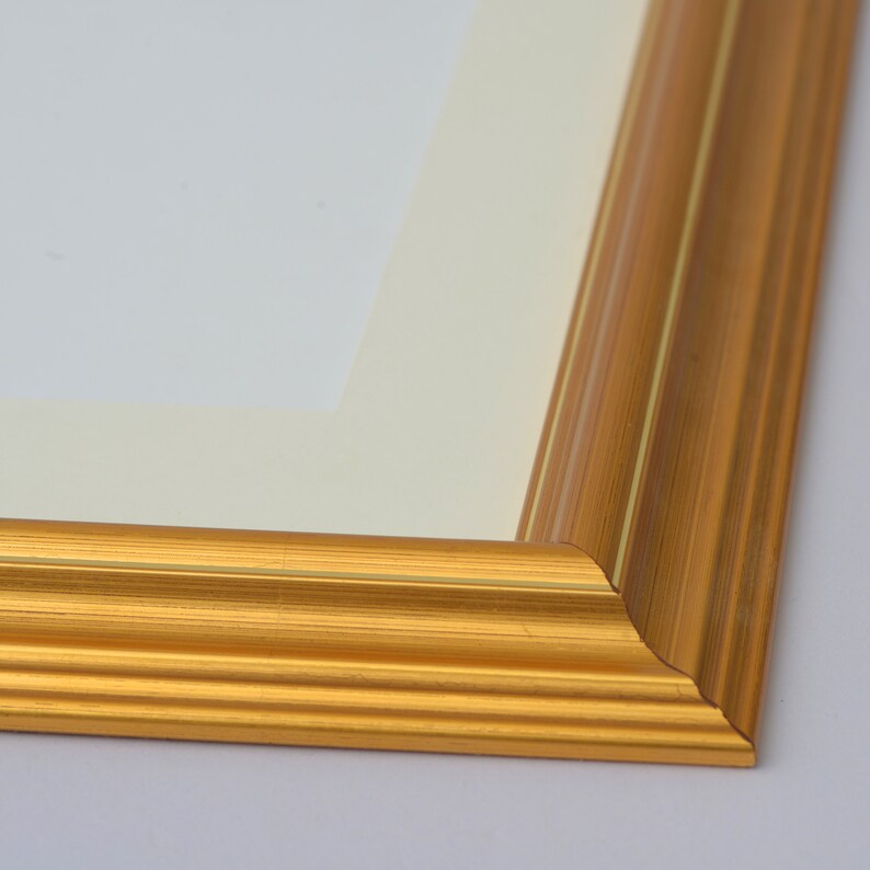 May include: Close-up of the corner of a gold picture frame with a raised edge and a thin, decorative line running along the edge.