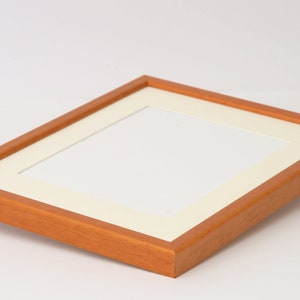 May include: A wooden picture frame with a light brown finish and a white mat. The frame is empty and ready for a photo.