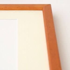 May include: A close-up of the corner of a wooden picture frame. The frame is a light brown color and has a smooth finish.
