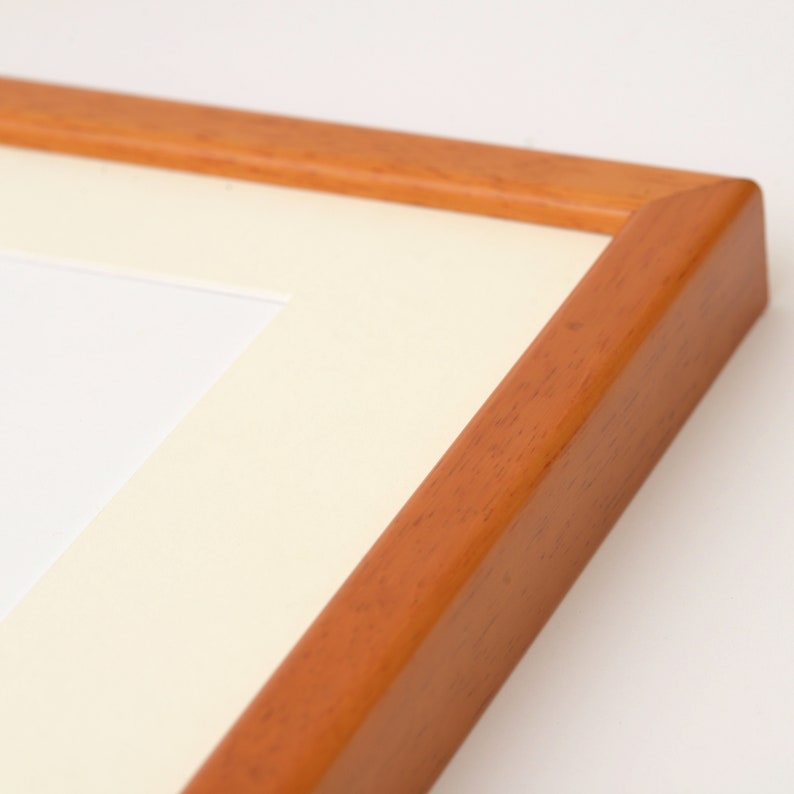 May include: A close-up of the corner of a wooden picture frame with a white mat. The frame is a light brown color and has a smooth finish.