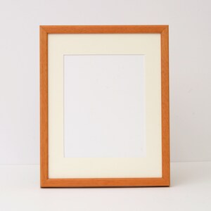 May include: A simple, wooden picture frame with a light brown finish. The frame has a white mat and is ready to display a photo or artwork.