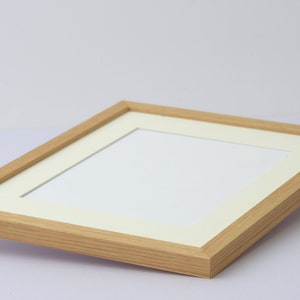 May include: A light-colored wooden picture frame with a white mat. The frame has a rectangular shape and a natural wood grain finish. The mat opening is also rectangular, designed to hold a photograph or artwork.