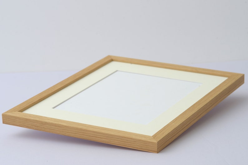 May include: A light-colored wooden picture frame with a white mat. The frame has a rectangular shape and a natural wood grain finish. The mat opening is also rectangular, designed to hold a photograph or artwork.