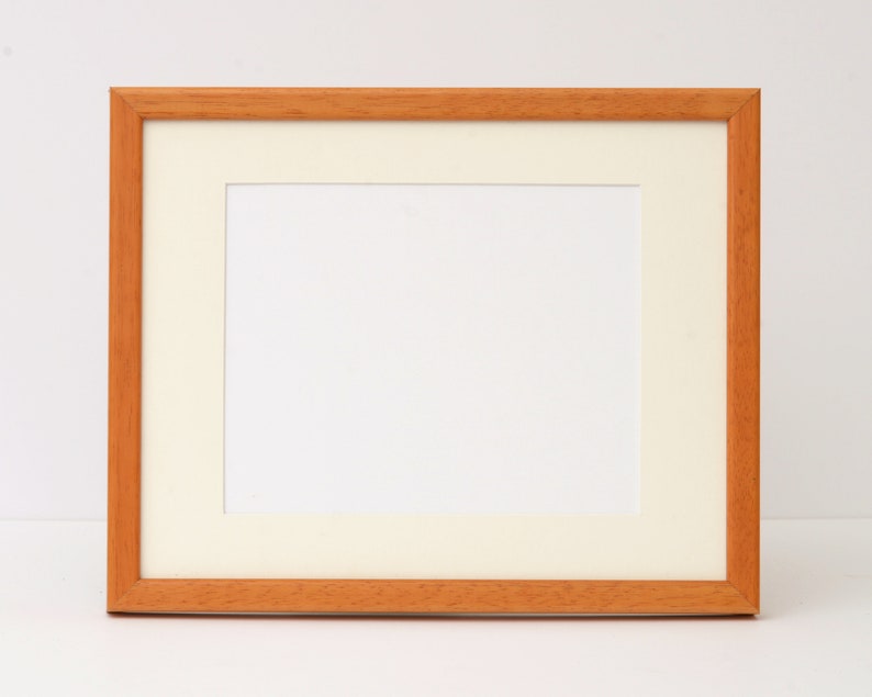 May include: A simple, wooden picture frame with a white mat. The frame is light brown and has a smooth finish.