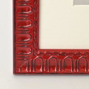 May include: Close-up of a red picture frame with a decorative, ornate design. The frame has a glossy finish and a slightly raised edge.