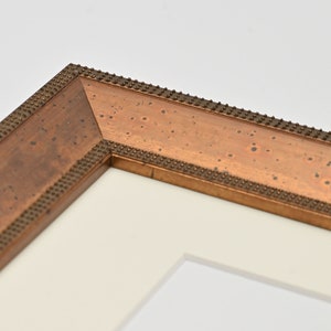 May include: Close-up of a corner of a picture frame with a gold-coloured wood frame and a white mount. The frame has a decorative beaded edge.