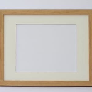 May include: A rectangular wooden picture frame with a light brown finish. The frame has a cream-colored mat and a white interior space for a photograph or artwork. The frame is designed for displaying images.