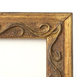 Peut inclure: Un cadre photo doré avec un design orné et sculpté. Le cadre est en bois et a une finition vieillie.