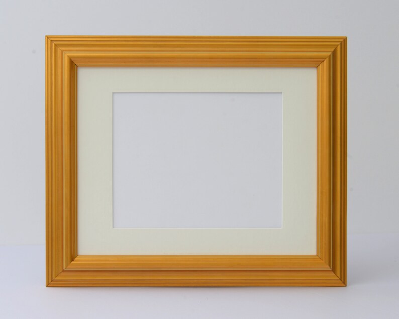 May include: A gold picture frame with a white mat. The frame has a simple, classic design.