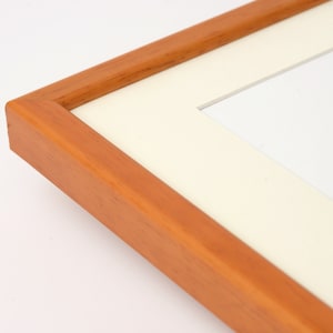 May include: A close-up of a wooden picture frame with a white mat. The frame is a light brown color and has a smooth finish.