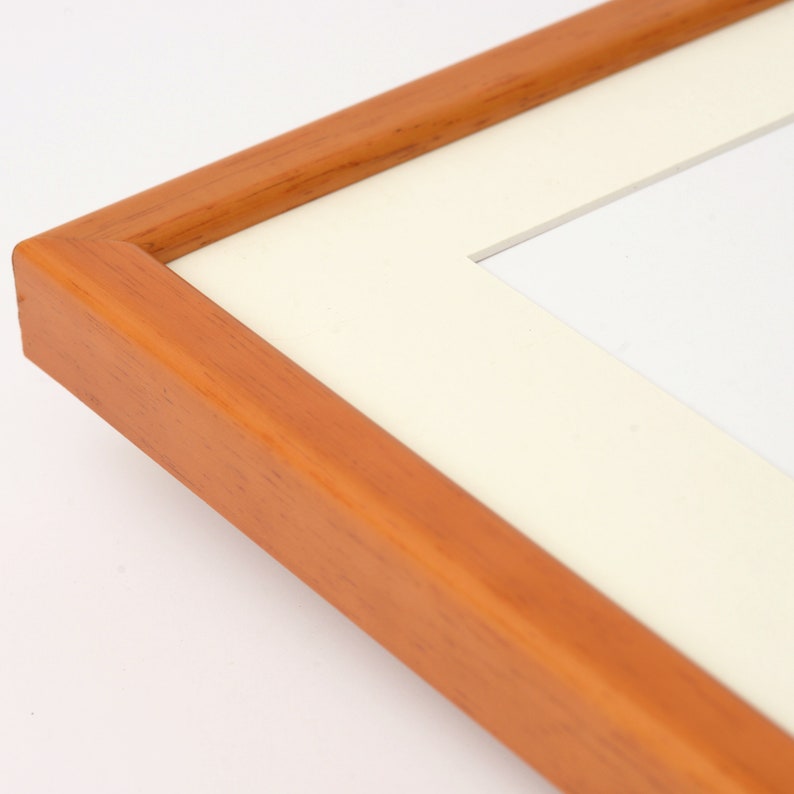 May include: A close-up of a wooden picture frame with a white mat. The frame is a light brown color and has a smooth finish.