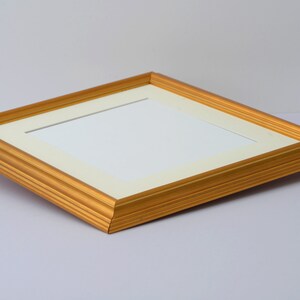 May include: A gold picture frame with a white mat. The frame has a simple, elegant design.