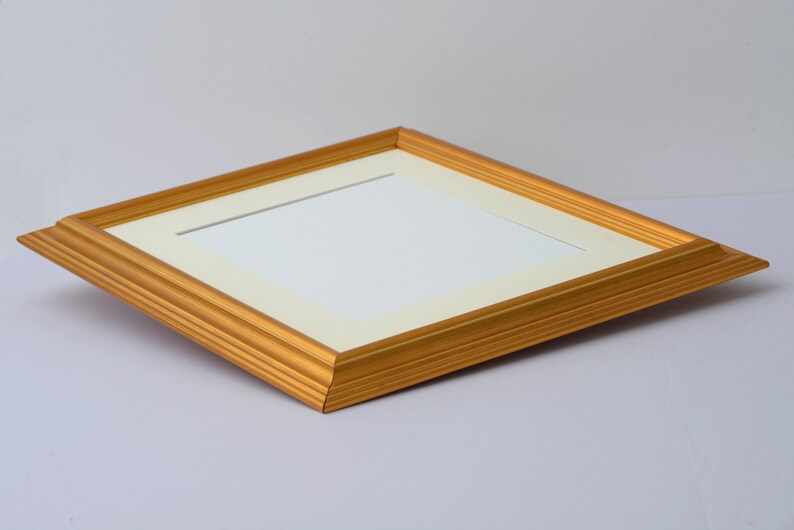May include: A gold picture frame with a white mat. The frame has a simple, elegant design.
