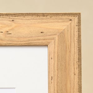 May include: Close-up of the corner of a natural wood picture frame. The frame has a light brown color and a slightly rough texture.