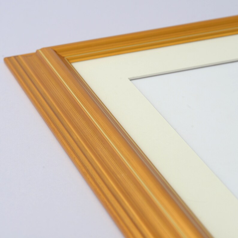 May include: A gold picture frame with a white mat. The frame has a simple, classic design.