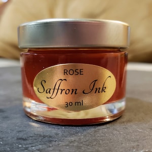 May include: A small glass jar of rose-colored ink labeled "Saffron Ink" with a gold oval sticker that says "ROSE" and "30 ml".