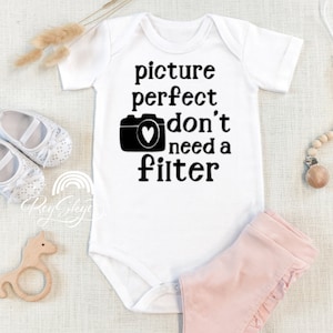 May include: White baby onesie with black text that reads "picture perfect don't need a filter" and a black camera with a heart inside.