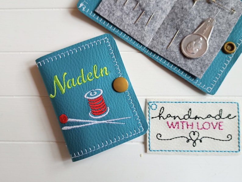 May include: Teal blue needle case with a gold button and embroidered text "Nadeln" and a spool of thread, needle and thread design.  A white tag with the text "handmade with love" is also shown.