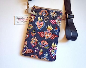 May include: A navy blue crossbody bag with a colourful embroidered heart pattern. The bag has a beige zip and trim, a black adjustable strap, and a small tag that says "handmade with love".