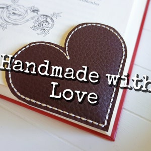 May include: A brown leather heart-shaped bookmark with white stitching and the text "Handmade with Love" in white.