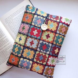 Könnte beinhalten: Ein farbenfroher, handgefertigter Buchumschlag mit Patchwork-Design. Der Umschlag zeigt Quadrate in verschiedenen Farben, darunter Rot, Blau, Gelb und Grün, mit einem Knopfverschluss. Das Etikett sagt "made with love".