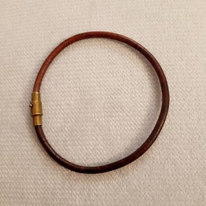 May include: A brown leather bracelet with a gold clasp.