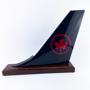 May include: A model airplane tail fin, navy blue with a red maple leaf emblem. The emblem is within a red circle. The model is mounted on a dark brown rectangular wooden base.