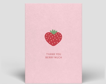 Puede incluir: Una tarjeta de felicitación de color rosa claro con una ilustración de una fresa roja con un tallo verde en la parte superior central. Debajo de la fresa, el texto THANK YOU BERRY MUCH está impreso en una fuente roja sencilla y clara.