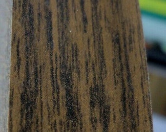 May include: A curved, vertical segment of a circular object featuring a brown wood grain pattern with dark brown, vertical streaks. The surface has a smooth, matte finish and a distinct, rounded edge that follows a gentle, sweeping arc.
