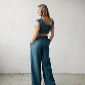 May include: A teal two-piece outfit featuring a crop top with a V-neck and button closure, paired with wide-leg pants. The outfit is made of a soft, flowing fabric, perfect for a casual, yet stylish look.