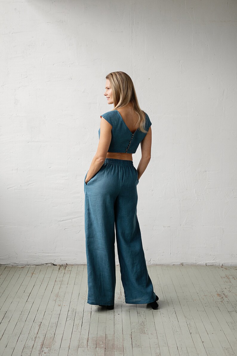 May include: A teal two-piece outfit featuring a crop top with a V-neck and button closure, paired with wide-leg pants. The outfit is made of a soft, flowing fabric, perfect for a casual, yet stylish look.