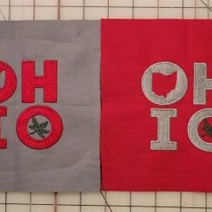 Puede incluir: Dos cuadrados de tela, uno gris y otro rojo, con la palabra "OHIO" bordada en rojo en el cuadrado gris y en plata en el cuadrado rojo. Ambos cuadrados presentan un contorno del estado de Ohio y una hoja de buckeye estilizada.