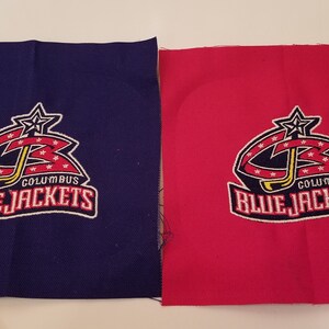 Puede incluir: Dos parches de tela con el logotipo de los Columbus Blue Jackets. El logotipo es rojo, blanco y azul con una estrella en la parte superior. Un parche está sobre un fondo azul y el otro sobre un fondo rojo.