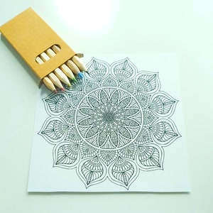 May include: A black and white mandala design on a white card with a set of colored pencils in a brown cardboard box.