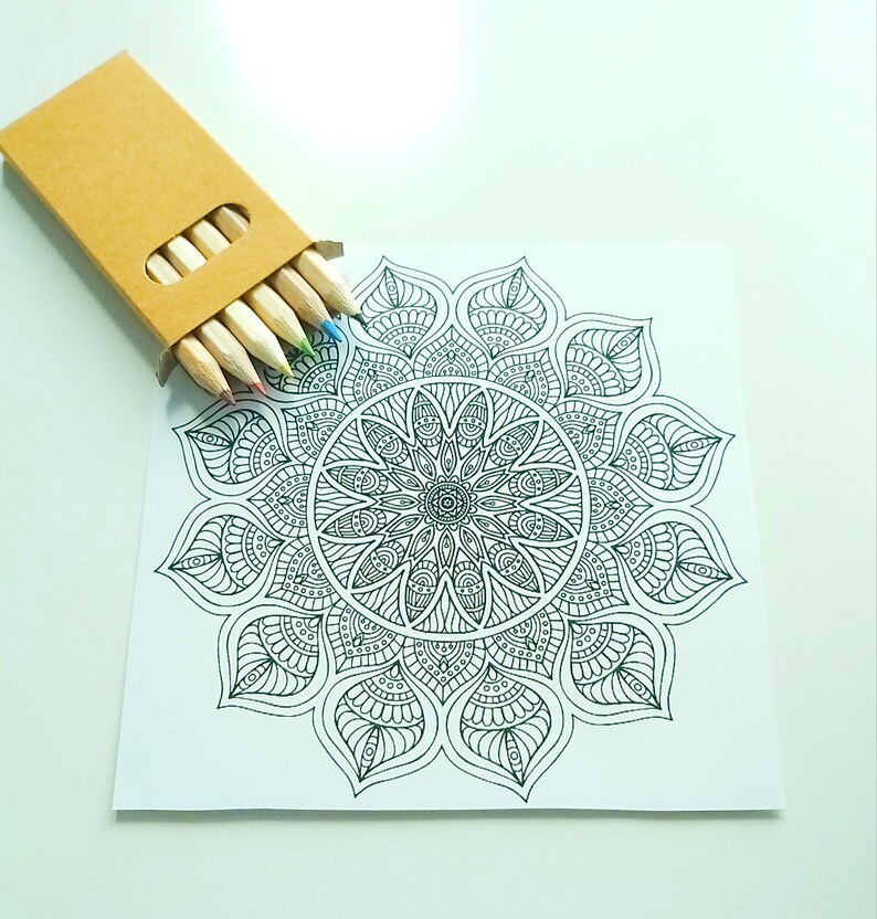 May include: A black and white mandala design on a white card with a set of colored pencils in a brown cardboard box.