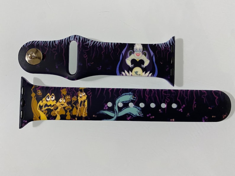 May include: A black and purple Apple Watch band with a graphic of Ursula from The Little Mermaid. The band has a dark background with purple lightning bolts and a scene of Ursula with her eels.