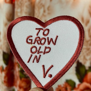 May include: Red heart-shaped patch with white fabric and red embroidered text that reads "To Grow Old In V."