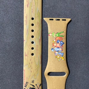 Puede incluir: Correa de reloj Apple Watch de color beige con un dise&ntilde;o de mapa y las palabras "Lost Boys" y "Never Land". La correa tambi&eacute;n presenta una ilustraci&oacute;n de Peter Pan y otros personajes. La correa est&aacute; hecha de un material flexible.