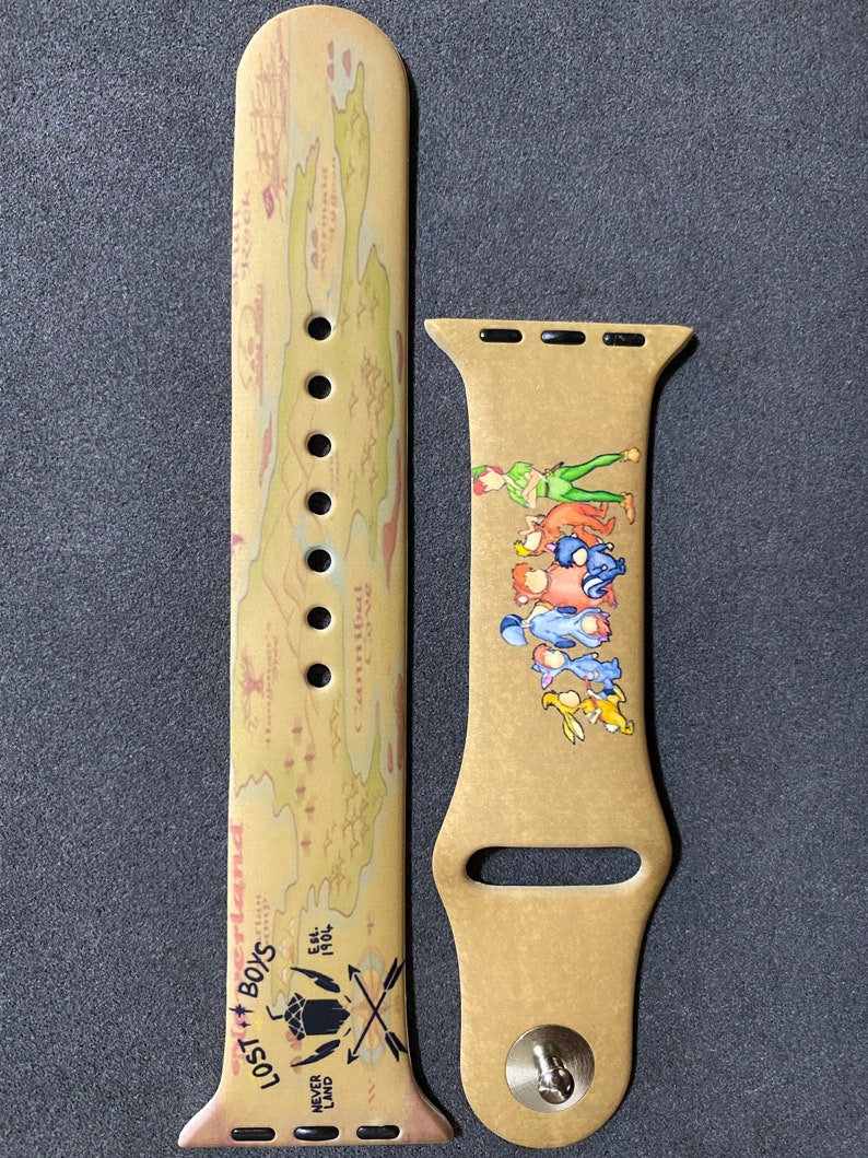 Puede incluir: Correa de reloj Apple Watch de color beige con un dise&ntilde;o de mapa y las palabras "Lost Boys" y "Never Land". La correa tambi&eacute;n presenta una ilustraci&oacute;n de Peter Pan y otros personajes. La correa est&aacute; hecha de un material flexible.