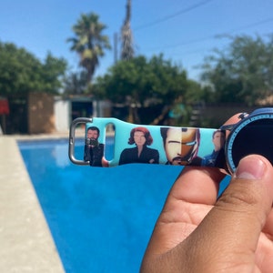 May include: A blue and white watch band with a printed image of characters from a popular superhero movie. The band is made of silicone and has a silver buckle.