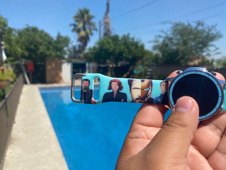 May include: A blue and white watch band with a printed image of characters from a popular superhero movie. The band is made of silicone and has a silver buckle.