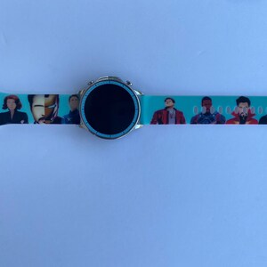 May include: A turquoise smartwatch band with a black screen and a print of various Marvel characters, including Iron Man, Black Widow, and Captain America.