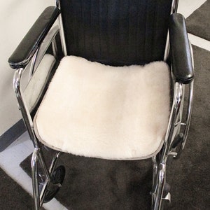 May include: A wheelchair with a black seat and backrest, chrome frame, and black armrests. A cream-coloured, fluffy cushion covers the seat. The footrests are silver.