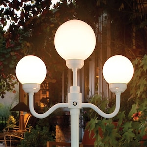 May include: White outdoor lamp post with three round globe lights. The lamp post is in a backyard setting with patio furniture.